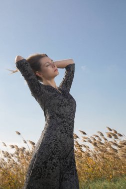 Çayırda poz veren siyah beyaz elbiseli kadın modelin seri fotoğrafları. Doğal ışıklandırmalı açık hava moda portresi.
