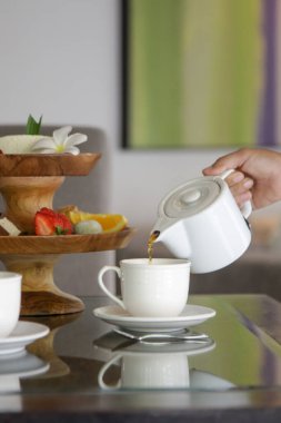 Çaydanlığı tutan ve beyaz seramik bir fincanda çay dolduran kadın.