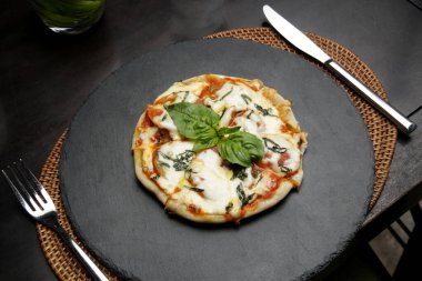 Pizza Margherita with with tomatoes, basil and mozzarella cheese on black stone tray.