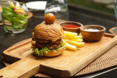 Small size burger served with french fries and sauces on the wooden board in cafe