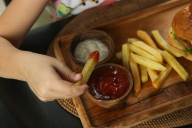 Little girl eating french fries with tomato sauce at the restaurant