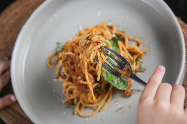 Little girl eating a portion of spaghetti bolognese at the restaurant