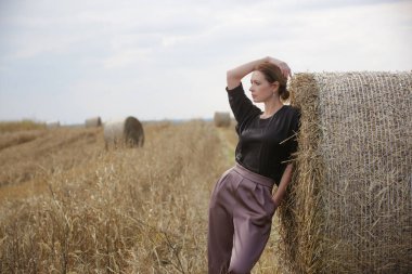 Sonbahar buğday tarlasında hasat sonrası şık genç bir kadının açık hava moda portresi.