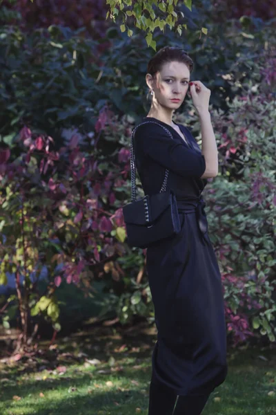 美丽的公园里穿着雅致典雅的黑色连衣裙的女人的户外肖像 秋季时装系列 — 图库照片