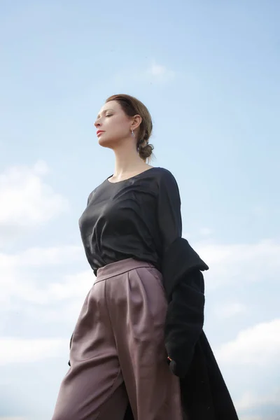 絹のブラウス ズボンと青い空に対するコートでスタイリッシュな若い女性の屋外ファッションの肖像画 — ストック写真