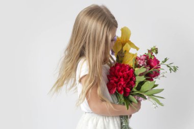 Stüdyo portresi. Güzel küçük bir kız. Elinde çeşitli çiçeklerden büyük renkli bir buket tutuyor..
