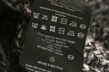 Kumaş kompozisyon etiketi, yıkama talimatları ve siyah kumaş etiketinde geri dönüşüm işareti. Elbiselerin üzerindeki çamaşırhane etiketi.