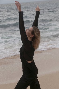 Issız okyanus sahillerinde siyah elbiseli genç bir kadının portresi, özgürlük kavramı ve harita dışı seyahat.