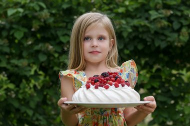 Çiçekli yaz elbisesi giymiş, elinde Pavlova pastası olan sevimli küçük bir kızın ön resmi.