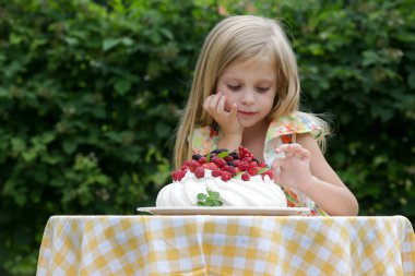 Çiçekli yaz elbisesi içinde Pavlova pastası yiyen sevimli küçük kız.