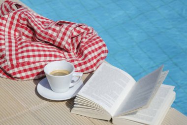 Açık bir kitap ve yüzme havuzunun yanında bir fincan kahve. Yaz günü eğlence konsepti