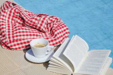 Açık bir kitap ve yüzme havuzunun yanında bir fincan kahve. Yaz günü eğlence konsepti