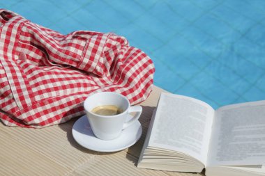 Açık bir kitap ve yüzme havuzunun yanında bir fincan kahve. Yaz günü eğlence konsepti