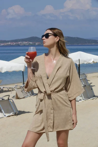 stock image Tourist woman in linen robe havin cocktail in a beach bar, relaxed solo vacation concept