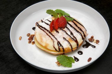 Kalın ve kabarık Amerikan krepleri çikolata şurubuna batırılmış taze çilek ve nane yapraklarıyla