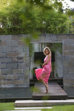 Açık hava portresi, tropikal tatil köyünde parlak pembe elbiseli şık bir kadın. Doğal ışık. Gündelik ama şık yaz kıyafetleri, bahar-yaz moda trendi, tropikal tatil tarzı.