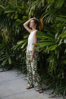 Açık hava portresi. Havalı, şık, keten elbiseli bir kadın. Tropikal bir tatil köyünde parkta. Doğal ışık. Gündelik ama şık yaz kıyafetleri, bahar-yaz moda trendi, tropikal tatil tarzı.