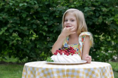 Çiçekli yaz elbisesi içinde Pavlova pastası yiyen sevimli küçük kız.