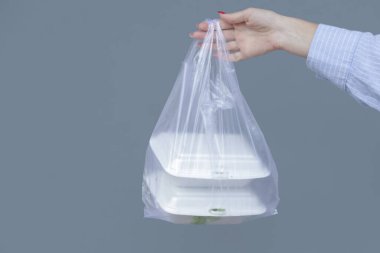 Woman's hands holding PVC plastic bag with takeaway foam lunch boxes. Single use food containers, donation concept.