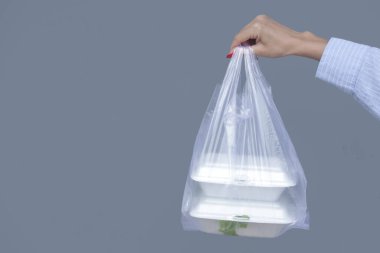Woman's hands holding PVC plastic bag with takeaway foam lunch boxes. Single use food containers, donation concept.