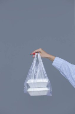Woman's hands holding PVC plastic bag with takeaway foam lunch boxes. Single use food containers, donation concept.
