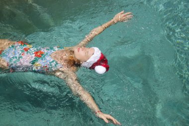 Noel Baba şapkalı genç bir kadın havuzda dinleniyor. Noel tropikal tatil konsepti.