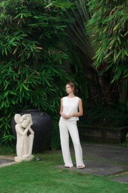 Açık hava portresi, tropikal tatil köyünde beyaz keten elbiseli şık bir kadın. Doğal ışık. Gündelik ama şık yaz kıyafetleri, bahar-yaz moda trendi, tropikal tatil tarzı