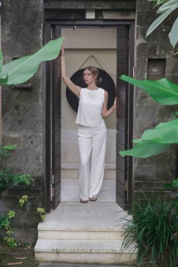 Açık hava portresi, tropikal tatil köyünde beyaz keten elbiseli şık bir kadın. Doğal ışık. Gündelik ama şık yaz kıyafetleri, bahar-yaz moda trendi, tropikal tatil tarzı