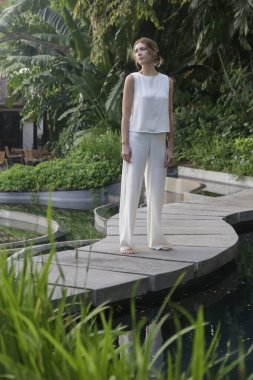 Açık hava portresi, tropikal tatil köyünde beyaz keten elbiseli şık bir kadın. Doğal ışık. Gündelik ama şık yaz kıyafetleri, bahar-yaz moda trendi, tropikal tatil tarzı