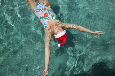 Noel Baba şapkalı genç bir kadın havuzda dinleniyor. Noel tropikal tatil konsepti.