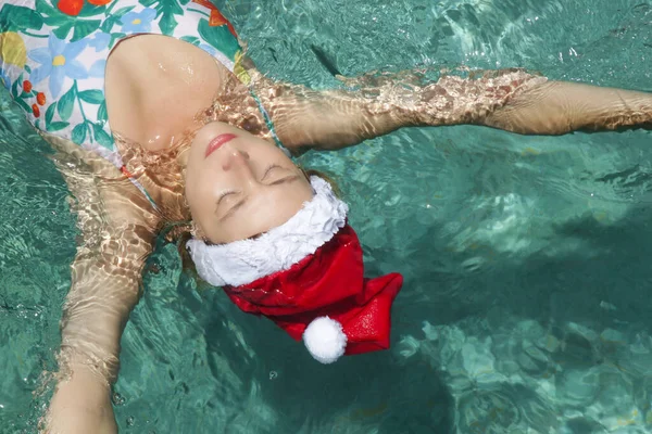 戴着桑塔帽的年轻女子在游泳池里放松 圣诞热带假期的概念 — 图库照片
