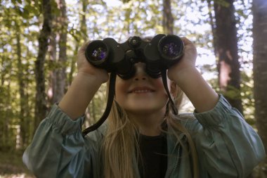 Dürbünle doğayı keşfeden sevimli küçük bir kız. Çocuk dışarıda oynuyor. Çocuklar seyahat, macera ve kuş izleme konsepti.