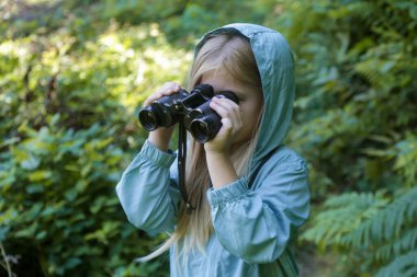 Dürbünle doğayı keşfeden sevimli küçük bir kız. Çocuk dışarıda oynuyor. Çocuklar seyahat, macera ve kuş izleme konsepti.