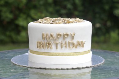 Sade ve zarif beyaz bir doğum günü pastası. Üstünde altın çiçekler var. 