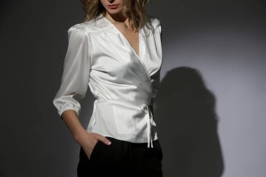 Şık siyah pantolon ve spot ışıkları altında beyaz ipek bluz giyen güzel bir kadın modelin moda portresi. Kadın güzelliği, moda ve cazibe kavramı.