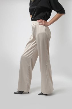 Stüdyo fotoğrafları, sade güzel kıyafetler, ipek saten siyah bluz ve beyaz geniş paça pantolon giyen genç kadın modeller.