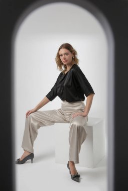 Stüdyo fotoğrafları, sade güzel kıyafetler, ipek saten siyah bluz ve beyaz geniş paça pantolon giyen genç kadın modeller.