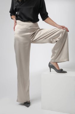 Stüdyo fotoğrafları, sade güzel kıyafetler, ipek saten siyah bluz ve beyaz geniş paça pantolon giyen genç kadın modeller.