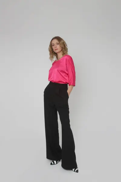 年轻女模特穿着简约漂亮的服装 丝绸缎子粉红衬衫和黑色宽腿裤的摄影棚照片系列 — 图库照片