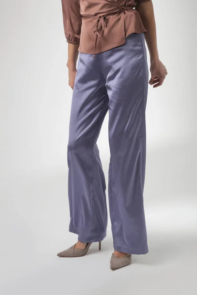 Serie of studio photos of young female model wearing simple beautiful outfit, silk satin brown blouse and lilac wide leg trousers