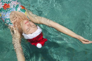 Noel Baba şapkalı genç bir kadın havuzda dinleniyor. Noel tropikal tatil konsepti.