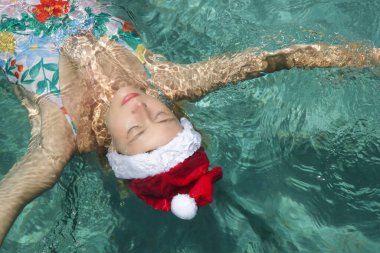 Noel Baba şapkalı genç bir kadın havuzda dinleniyor. Noel tropikal tatil konsepti.