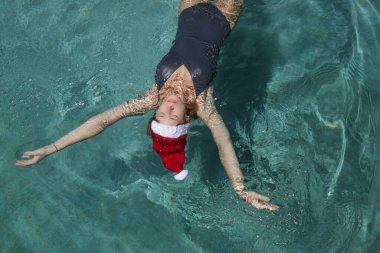 Noel Baba şapkalı genç bir kadın havuzda dinleniyor. Noel tropikal tatil konsepti.