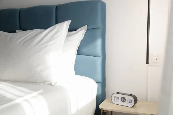 青いキングサイズのベッド クリスピーな白い寝具とデジタルアラームクロック 美しい朝の日の光の下でナイトスタンド — ストック写真