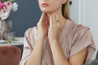 Beyaz kadın boğazına dokunuyor. Boğaz ağrısı, soğuk algınlığı, grip, bademcik iltihabı veya tiroid bezi sorunu