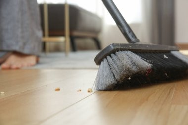 Ev temizliği. Ev işi yapan, elinde süpürge tutan ve yerleri süpüren bir kadın.