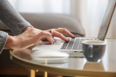 Oturma odasındaki sehpanın üstünde dizüstü bilgisayarda yazan kadın elleri.