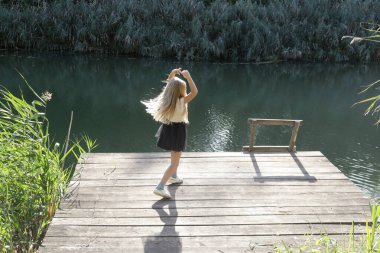 Sevimli sarışın kız gün ışığında rıhtımda dans ediyor. Doğada huzurlu bir yaz günü.