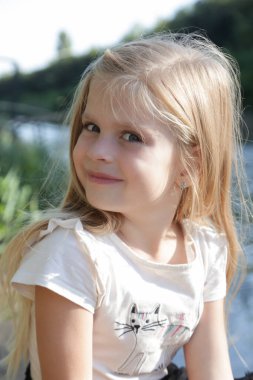 Uzun sarı saçlı sevimli bir anaokulu kızının portresi. Doğada huzurlu bir yaz günü..
