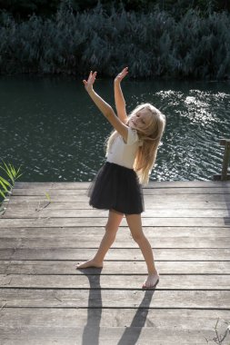 Sevimli sarışın kız gün ışığında rıhtımda dans ediyor. Doğada huzurlu bir yaz günü.